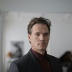 Confident businessman in a formal suit posing indoors with a serious expression.
